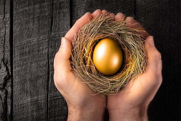 Protecting-Hands-Holding-Golden-Nest-Egg-On-Wooden-Table---Investment-Protection-Concept